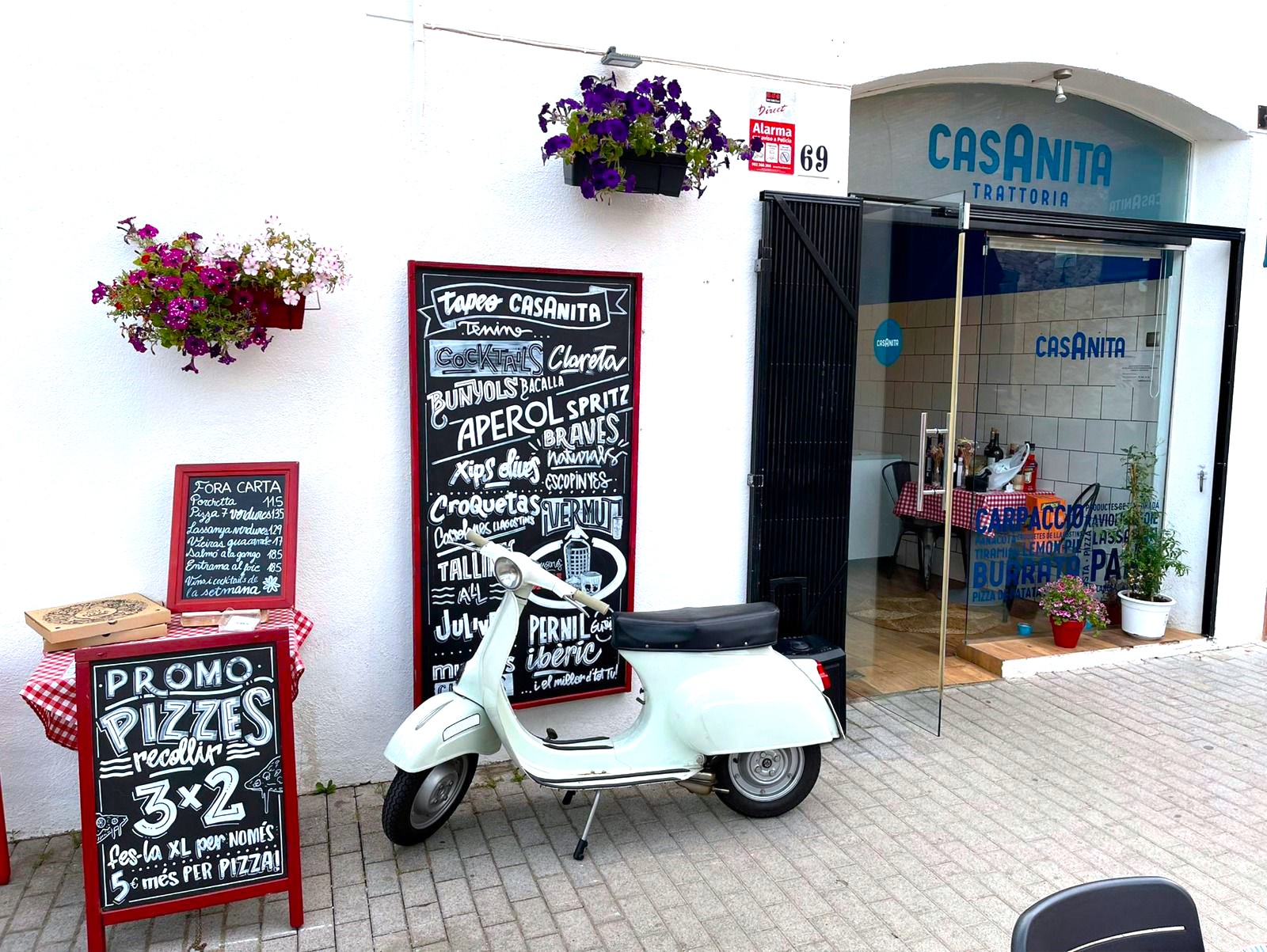 Fachada de Casanita a mediodía, con la Vespa blanca y las flores