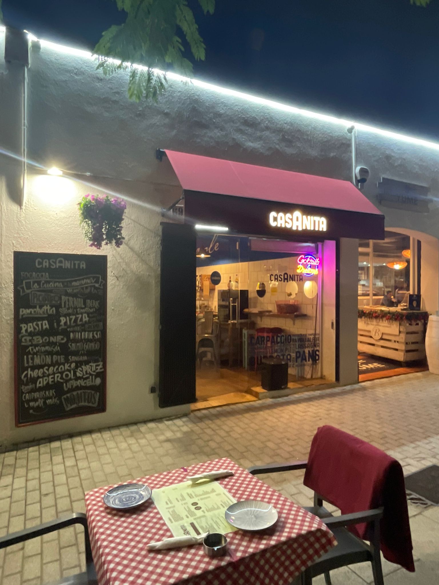 Casanita de noche, con el toldo granate y una mesa de terraza preparada